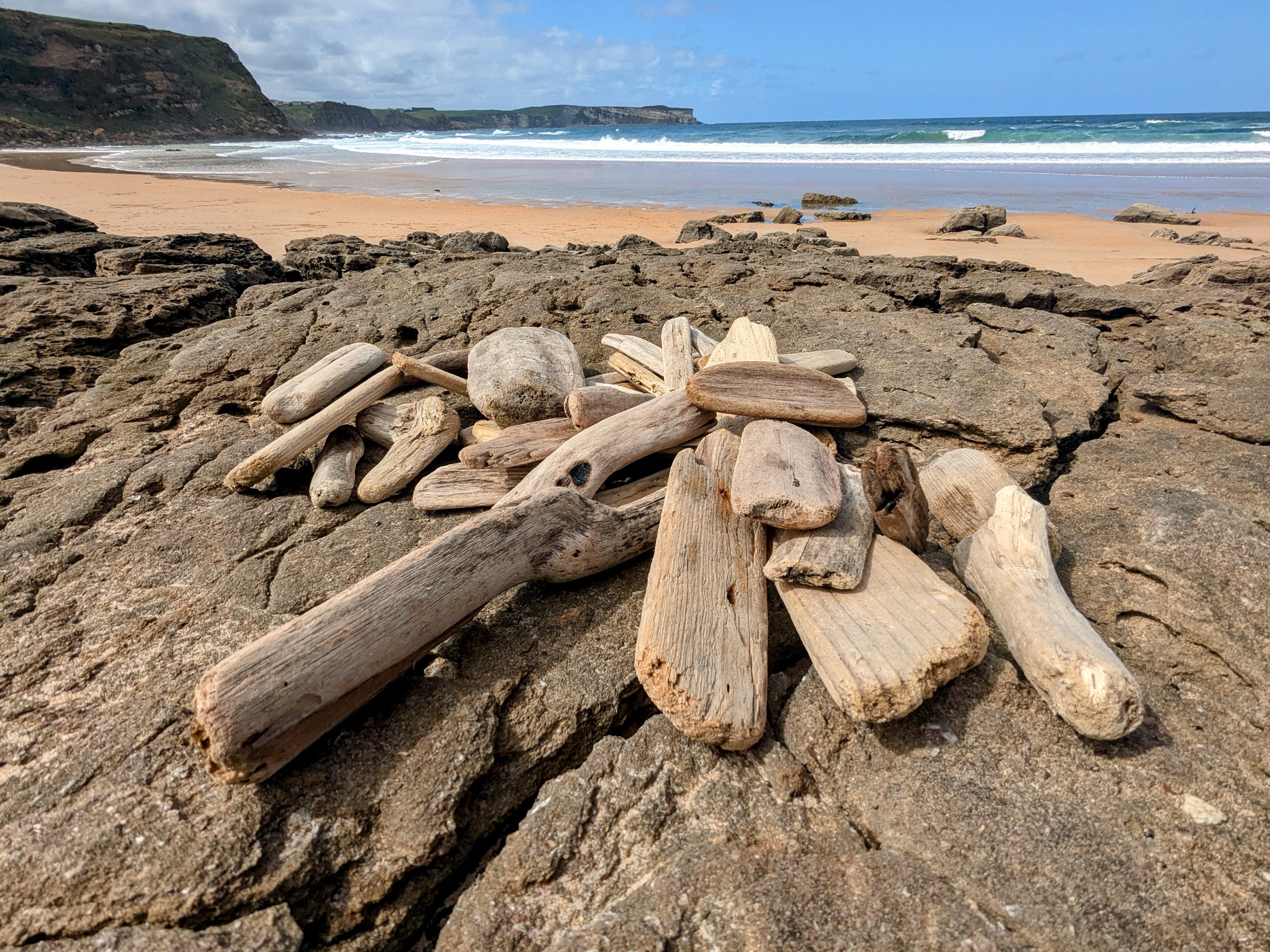A pile of sea-shaped driftwood pieces gathered on a rock on a Cantabrian beach — the raw material for the engraved room keys.